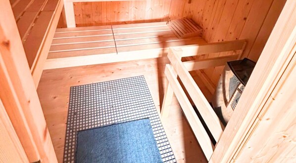 Saunahuone, jossa on puiset lauteet, matto ja lämmityselementti.
