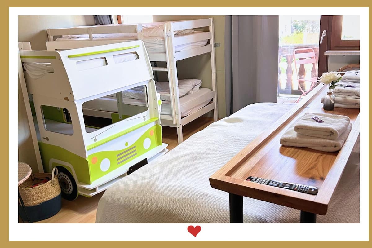 A children's playroom with bunk beds, a toy bus, and a table with towels and a remote control.