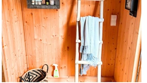 Une cabine de sauna en bois, avec une échelle en bois, une serviette bleue et un panier tressé.