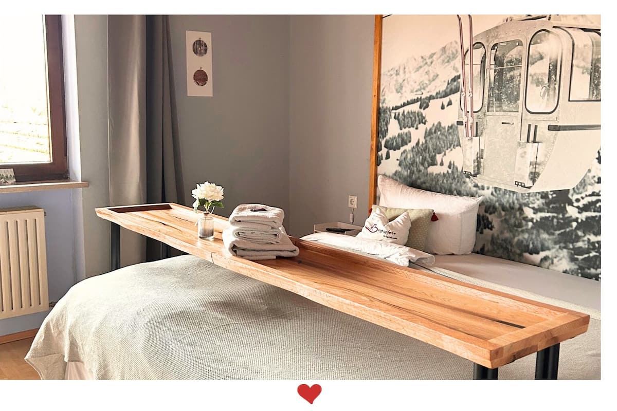 A neatly made bed with a wooden bedside table, a small vase with flowers, and a pillow with a heart design.
