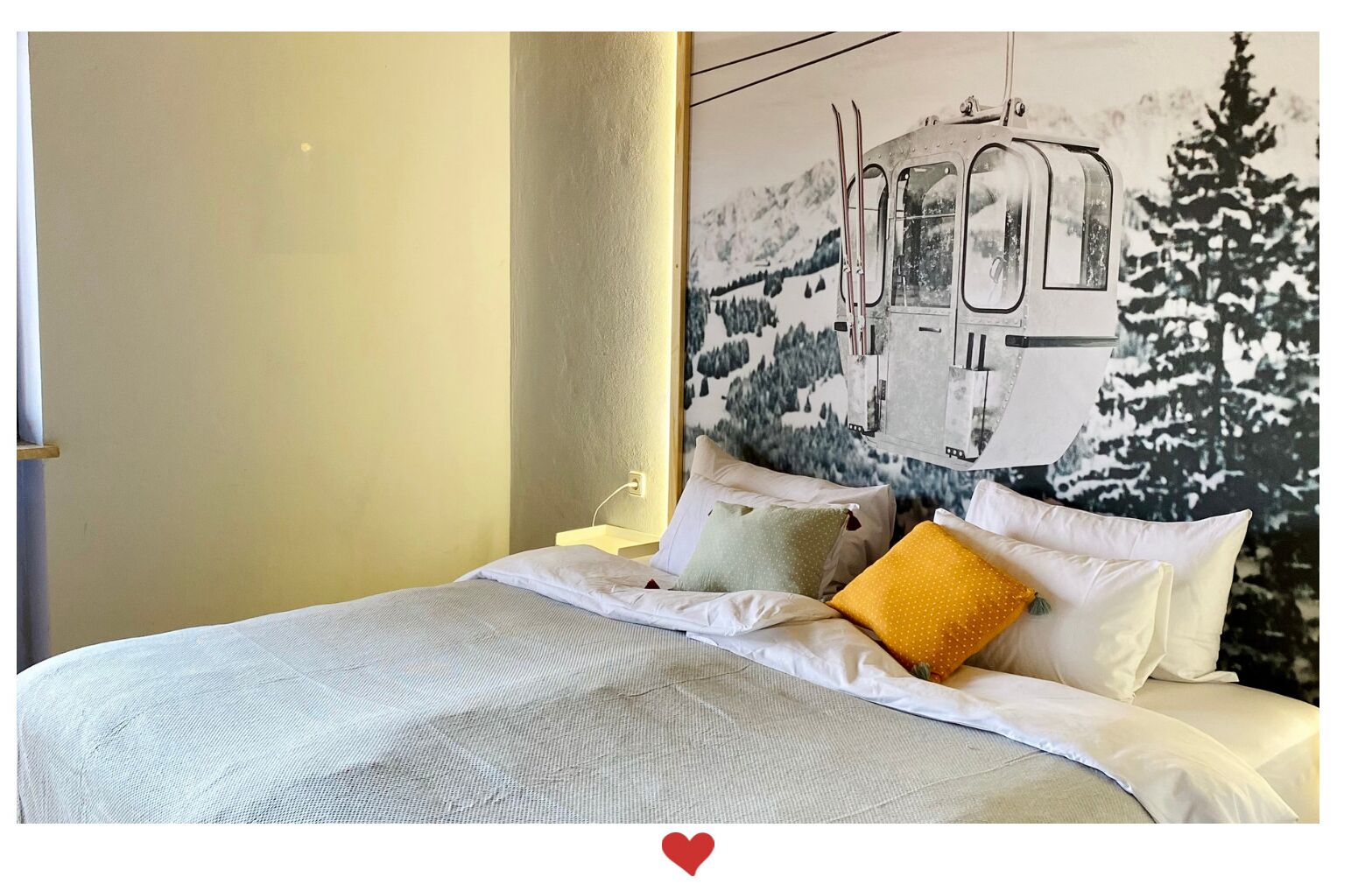 Habitación de hotel con cama, almohadas y un cuadro colgado en la pared que muestra un telesilla.