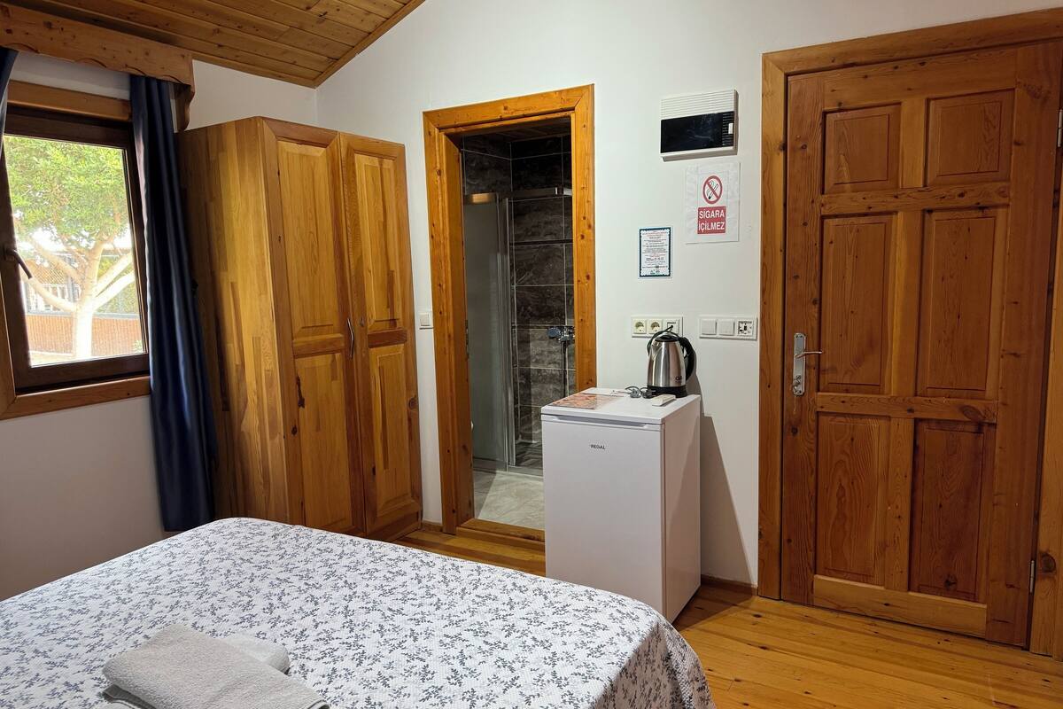 Ein Schlafzimmer mit Holztüren, einem Bett mit Blumenmuster-Bettwäsche, einem kleinen weißen Gerät und einem Fenster mit Vorhängen.