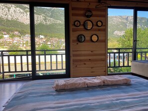 Una stanza con un letto, una parete in legno con specchi e un balcone affacciato su un villaggio e montagne.