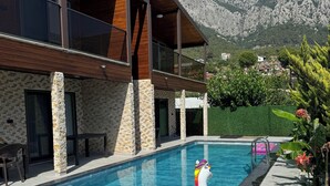 Un edificio moderno con piscina, pilares de piedra y vistas a las montañas.