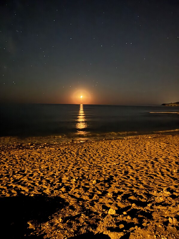 A beach at night with a calm sea reflecting the moonlight.