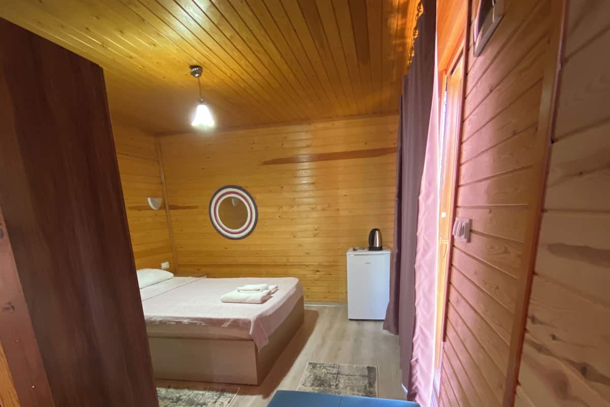 Ein kleiner, gemütlicher Raum mit Holzwänden und einem Einzelbett. Es steht ein kleiner Tisch mit einem Wasserkocher und ein Spiegel an der Wand.