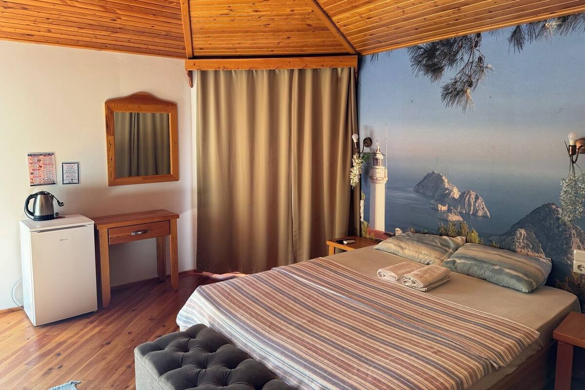 Ein Schlafzimmer mit Holzbalkendecke, einem Bett mit gestreifter Bettwäsche, einem Schreibtisch mit Wasserkocher und einem Gemälde eines Leuchtturms.