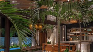 A modern indoor space with a dining area, seating, and a kitchen area. - Cala Blanca (Munggu)