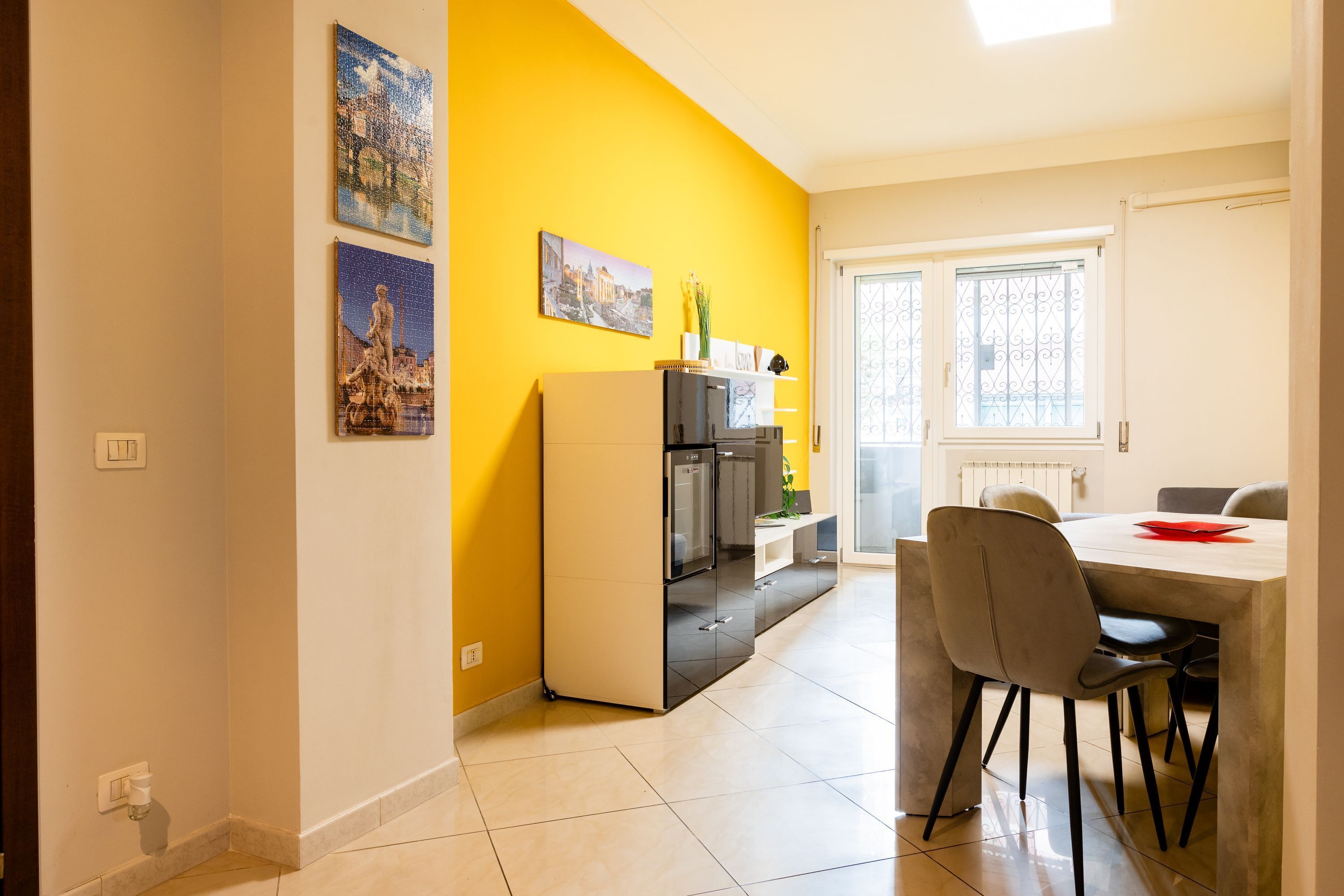A modern kitchen with a yellow accent wall, a dining area with a table and chairs, and a refrigerator.
