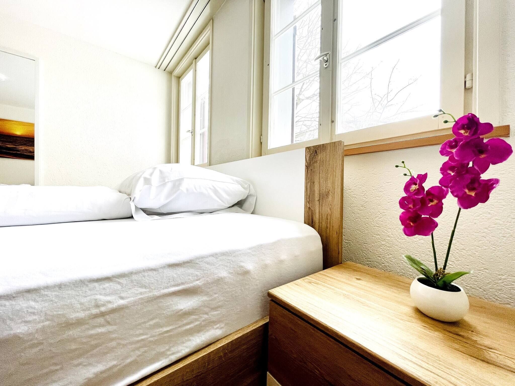 Una camera da letto con un letto, un comodino in legno e una finestra vista alberi.