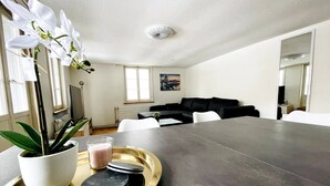 A modern living room with a large dining table, a potted orchid, and a tray with a glass of milk and coasters. - Beautiful Old Building Apartment In The Center (St. Gallen)