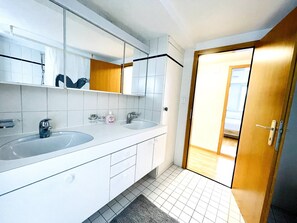A modern bathroom with two sinks, a large mirror, and a wooden door leading to another room.