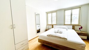 A bedroom with a wooden bed, white walls, a wardrobe, and a window with a view. - Beautiful Old Building Apartment In The Center (St. Gallen)