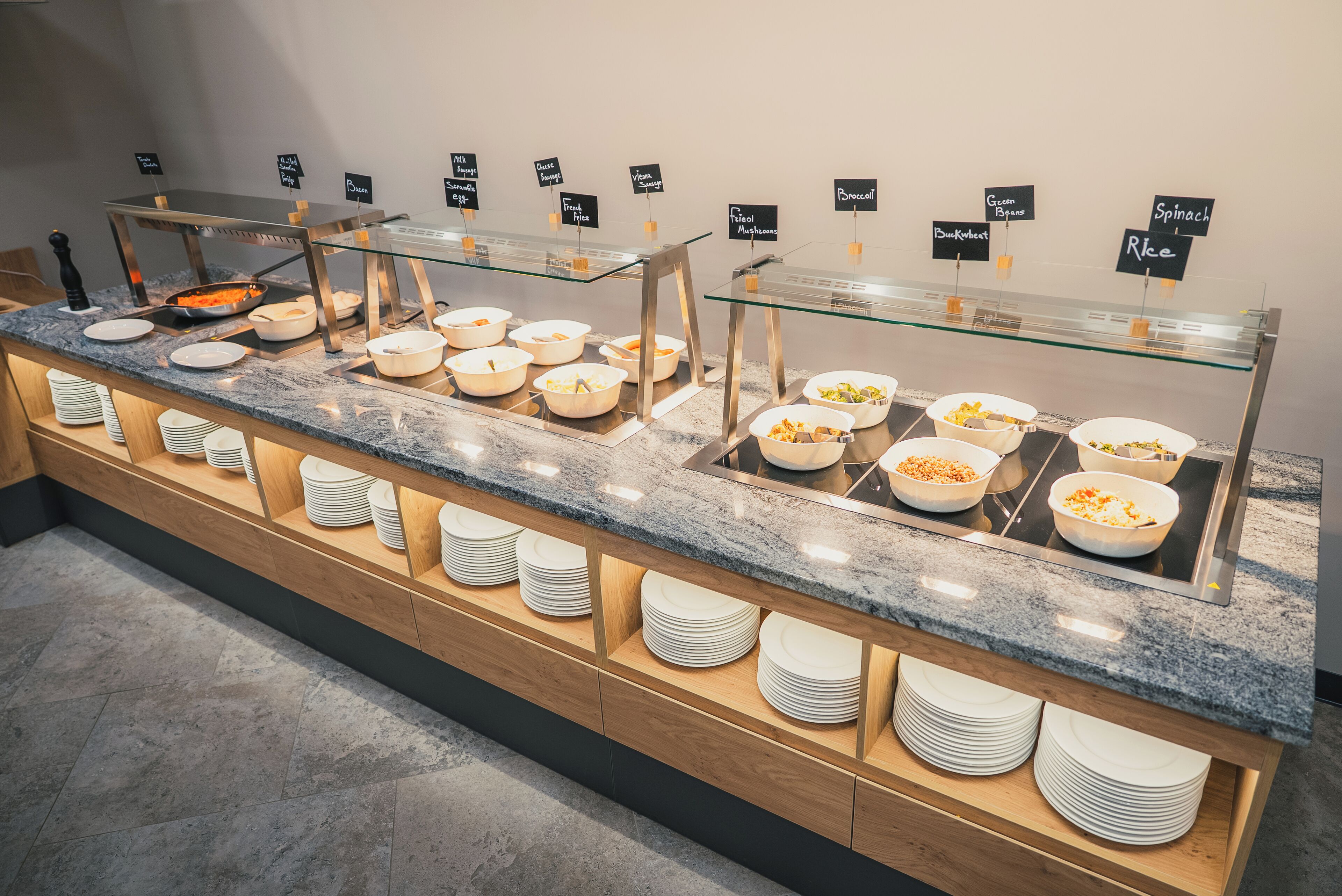 Een buffetopstelling met diverse food stations, aangeduid met gerechten zoals 'Spinazie', 'Rijst' en 'Champignons'.