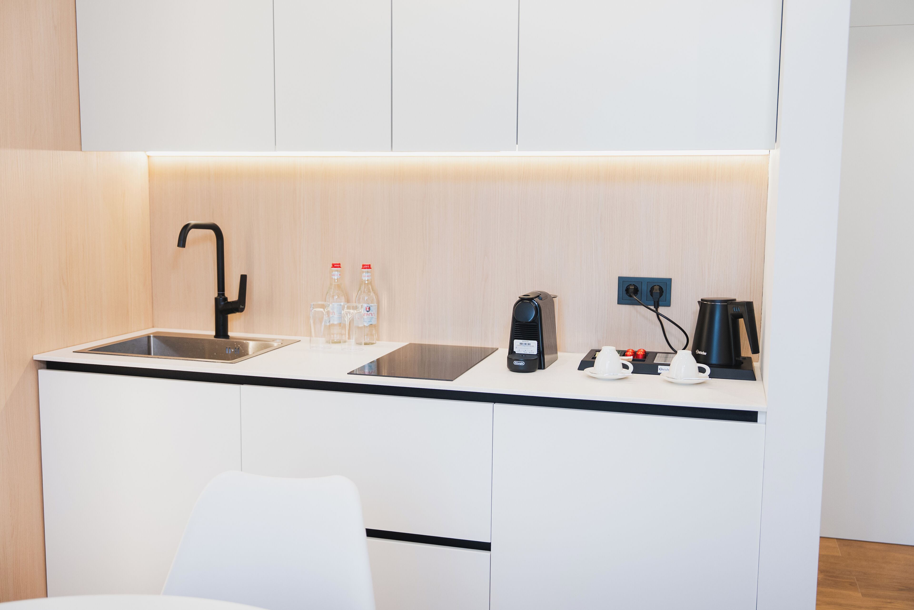 A compact kitchenette with a sink, two bottles of water, a coffee maker, and a kettle.