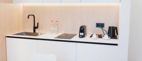 A compact kitchenette with a sink, two bottles of water, a coffee maker, and a kettle.