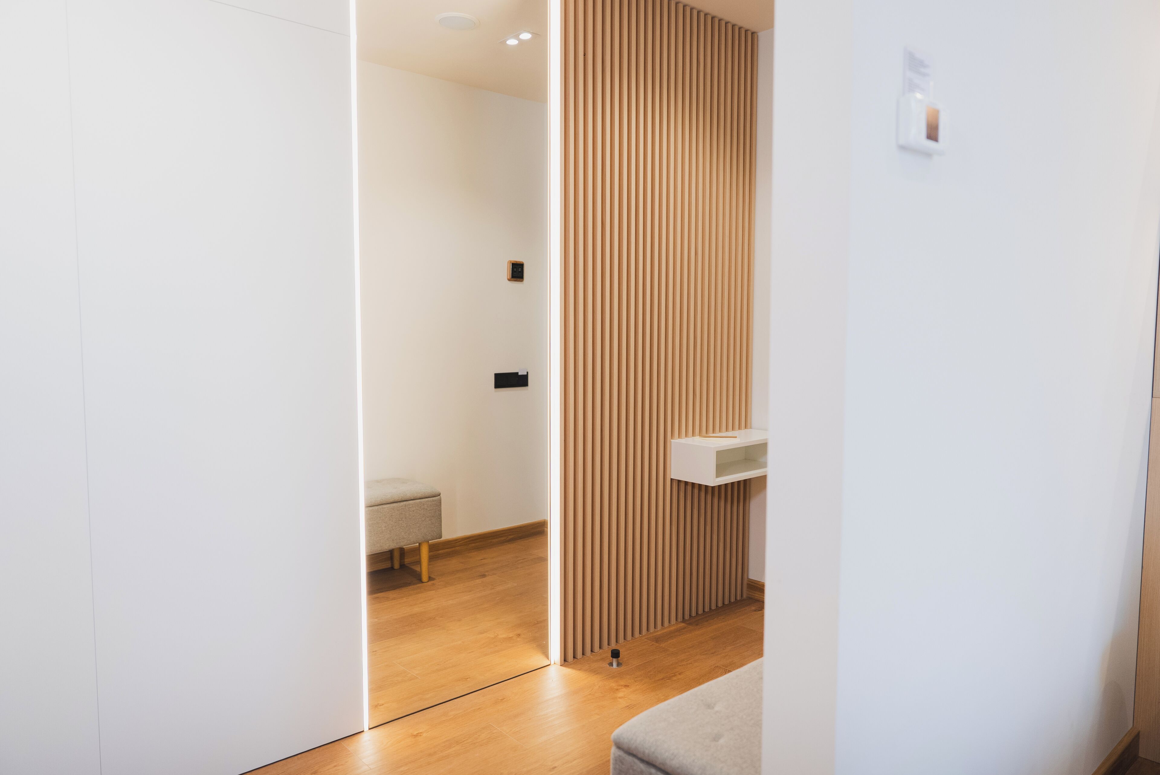A modern bathroom with a wooden panel divider, a bench, and a white sink.