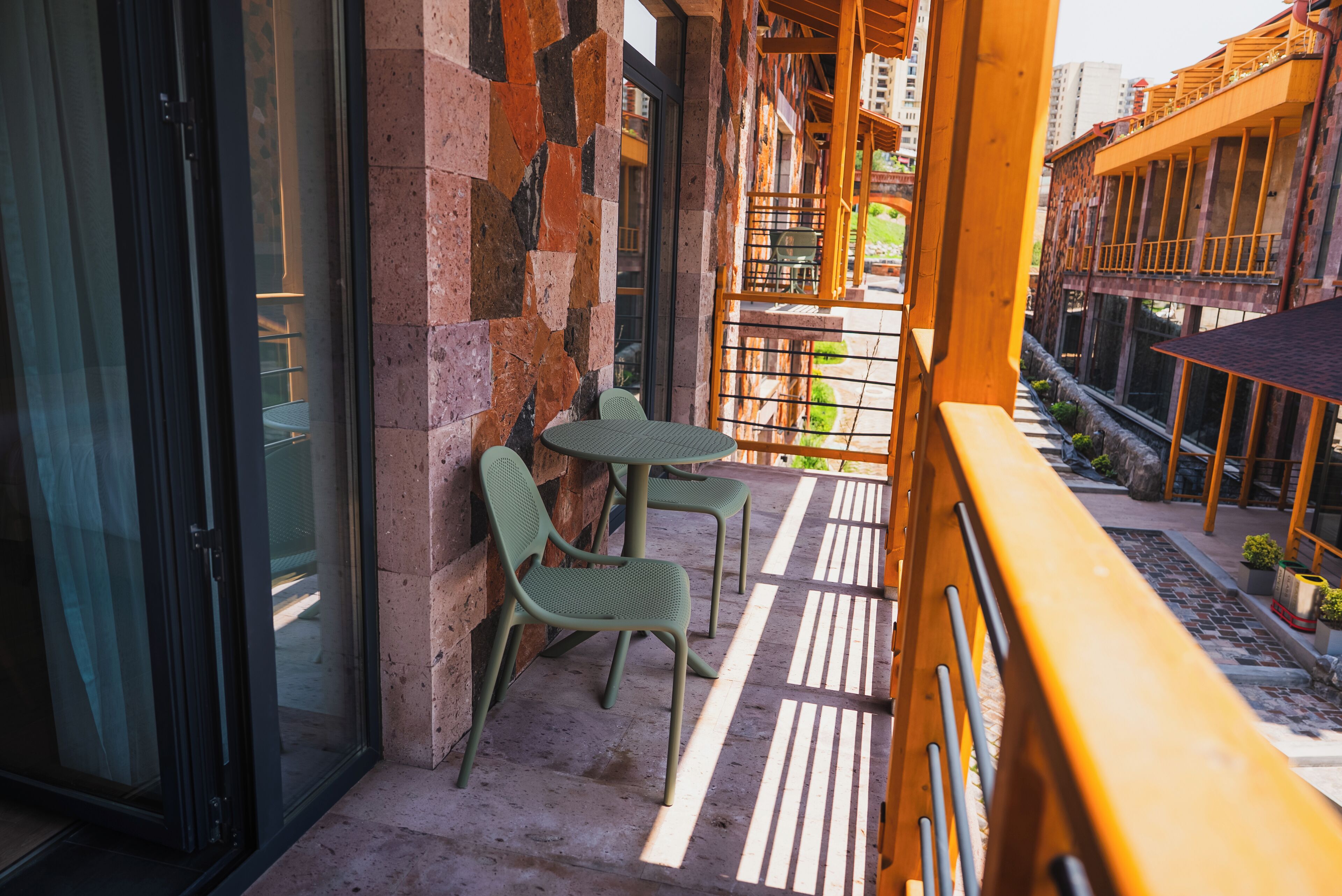 A balcony with two chairs and a table, a glass door, and a view of a building with a balcony.