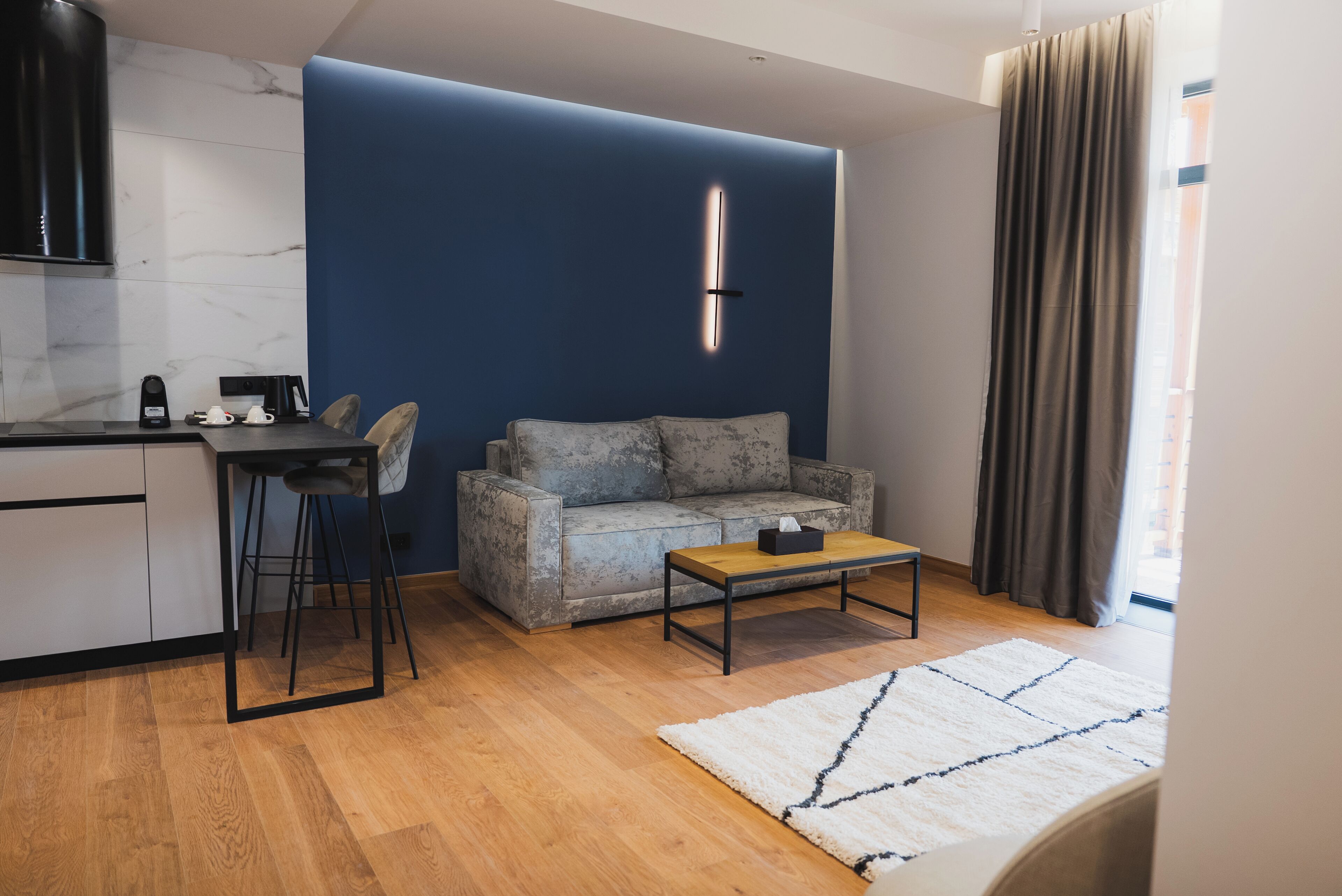 Una sala de estar moderna con sofá, una mesa de centro, una zona de cocina con estufa y una pared de acento azul.