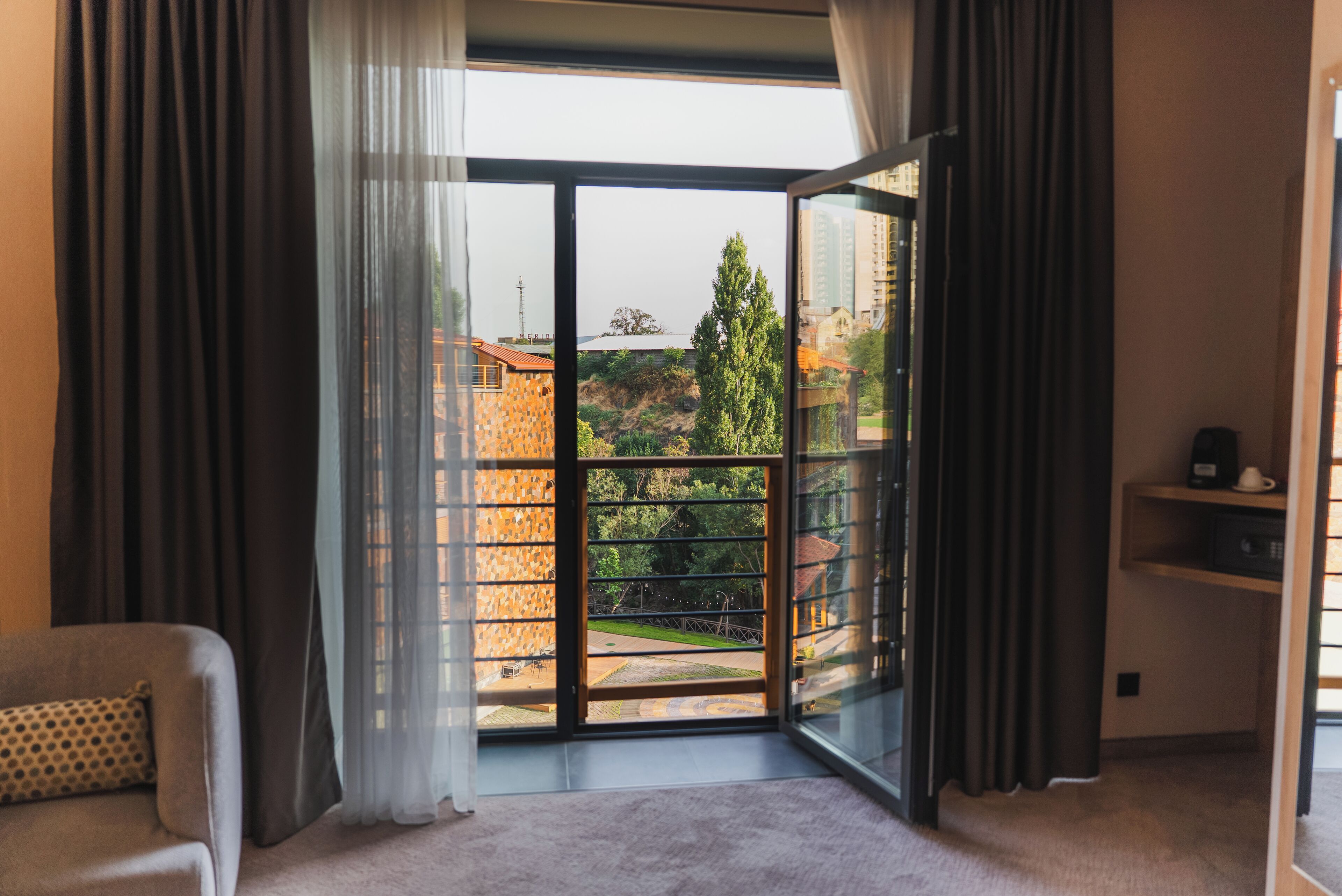 Una habitación con un amplio ventanal corredera que da a un balcón con vistas a edificios y árboles.