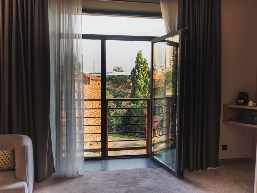 Una habitación con un amplio ventanal corredera que da a un balcón con vistas a edificios y árboles.