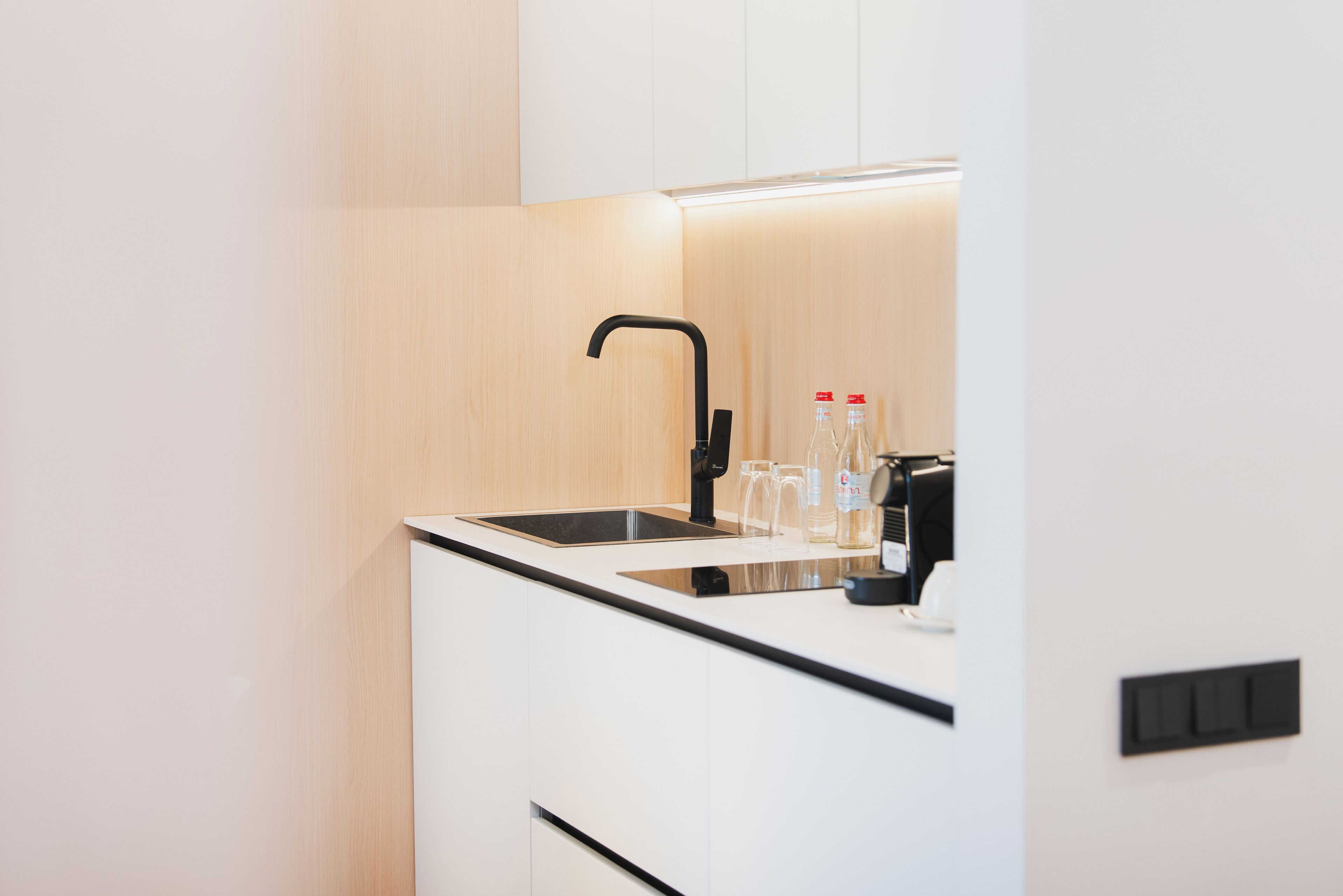 A modern kitchen with a black faucet, a sink, and a countertop with two bottles and a glass.