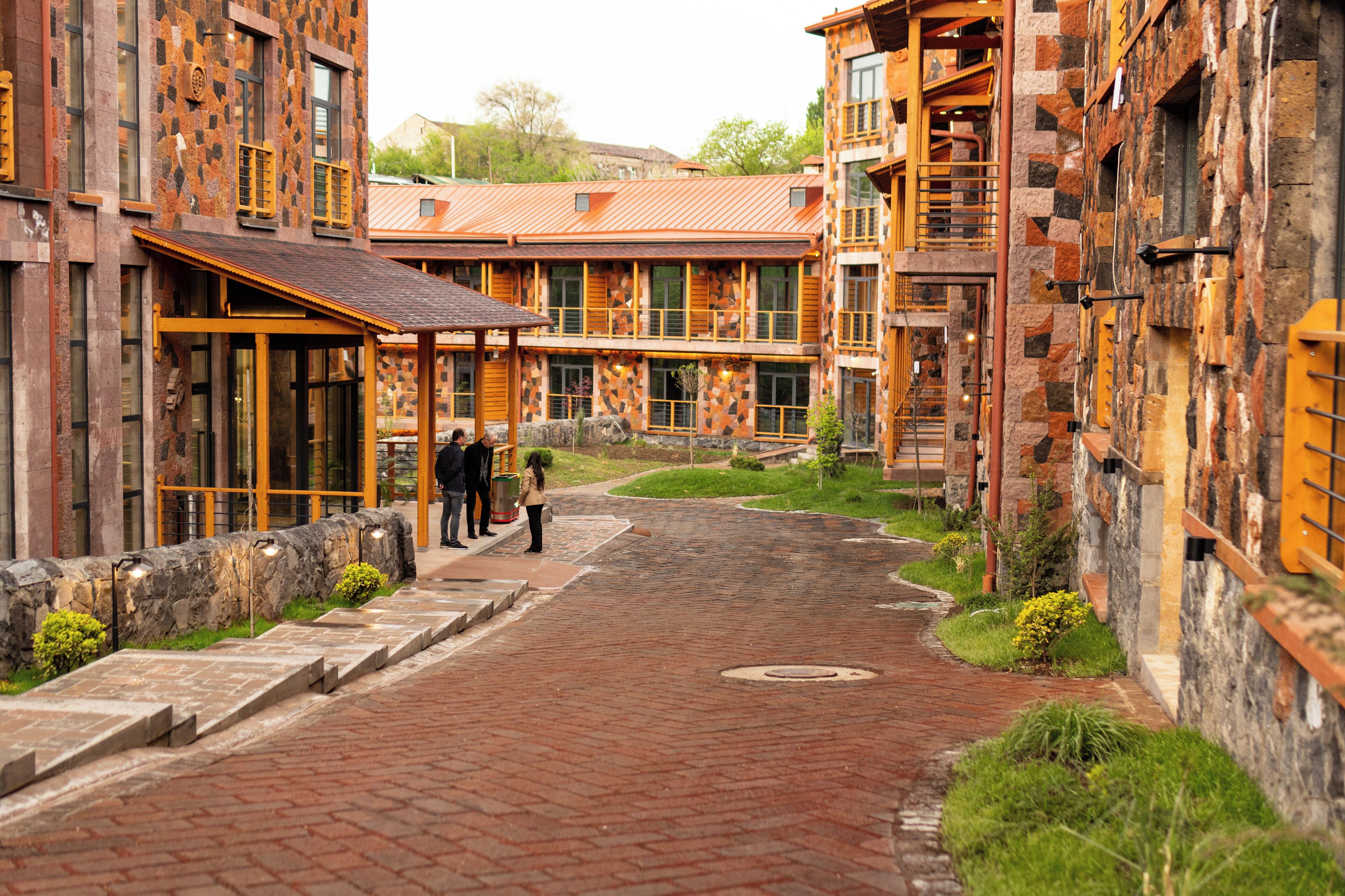A courtyard with a brick pathway, stone walls, and wooden buildings with large windows and balconies.