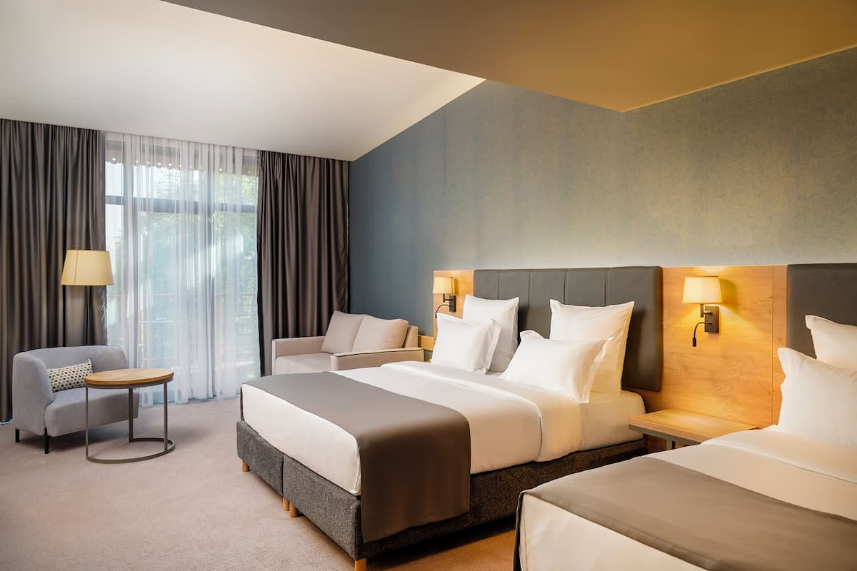 A hotel room with two beds, a sofa, a small table, and a lamp.