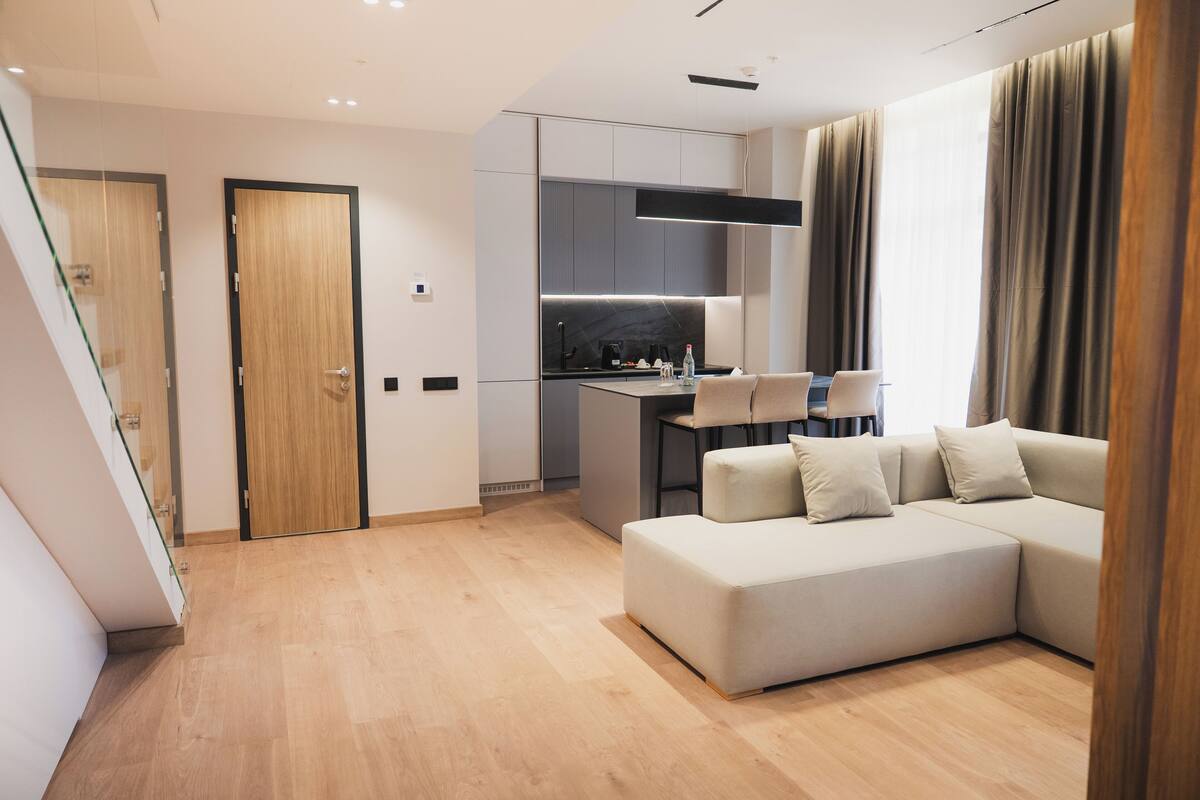 A modern living room with a sectional sofa, a dining area with a table and chairs, and a kitchen with a built-in island.