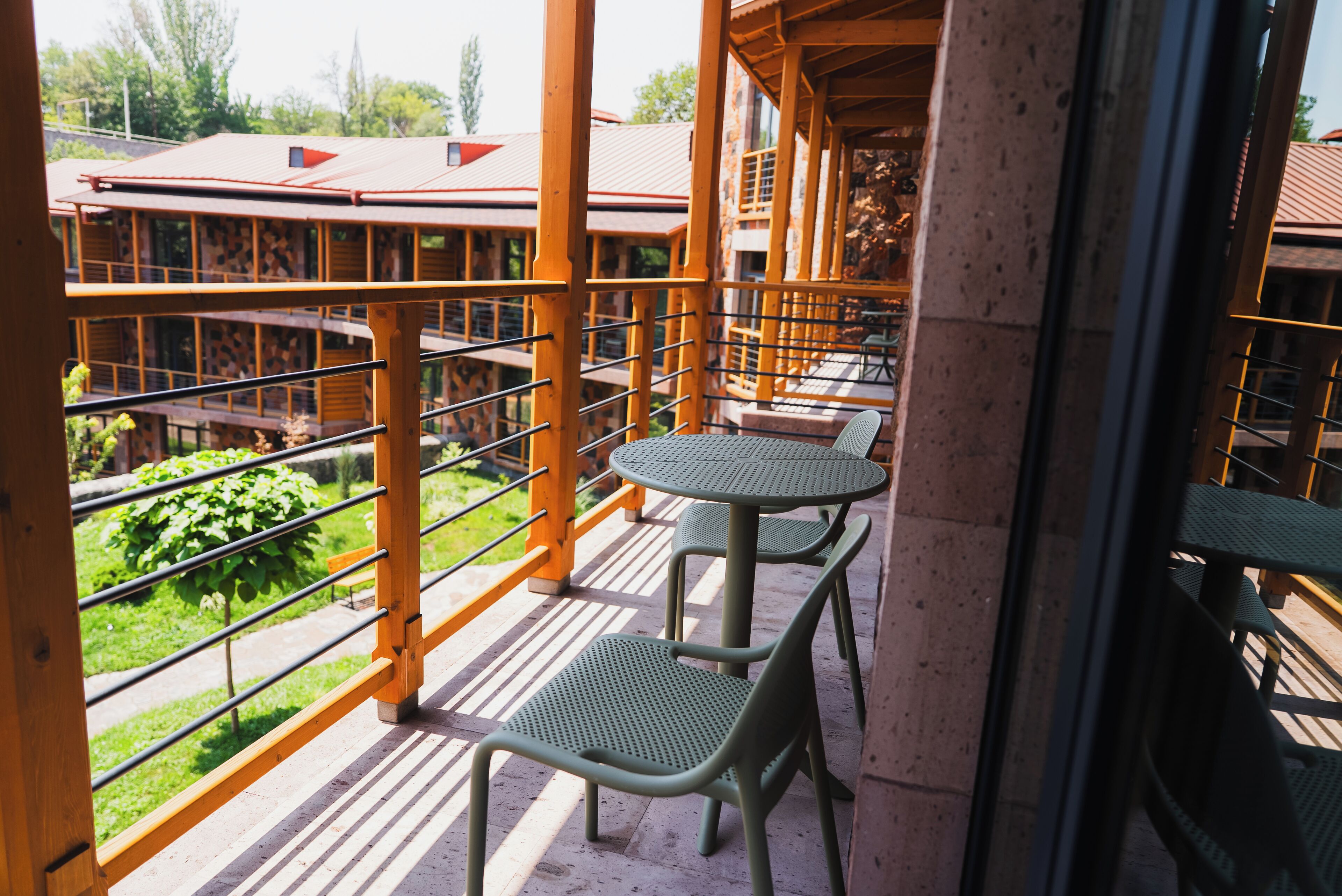 Un balcon avec deux tables et des chaises, une vue sur un immeuble avec un toit rouge et une pelouse verdoyante.