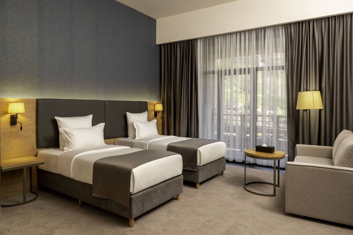 A hotel room with two beds, a sofa, a small table, and a lamp.
