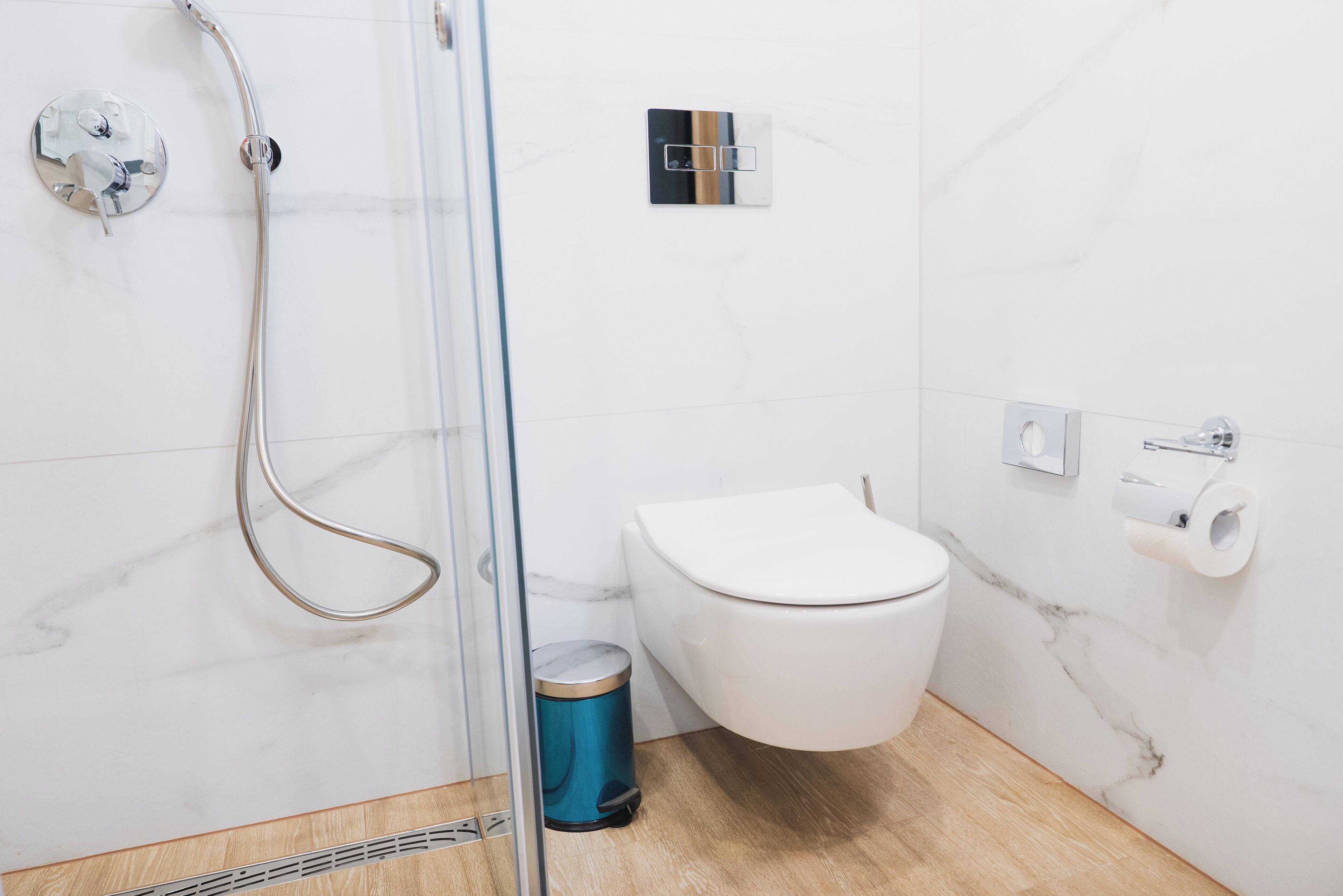 Een badkamer met douche, toilet en prullenbak.