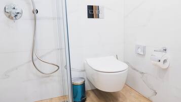 Een badkamer met douche, toilet en prullenbak.