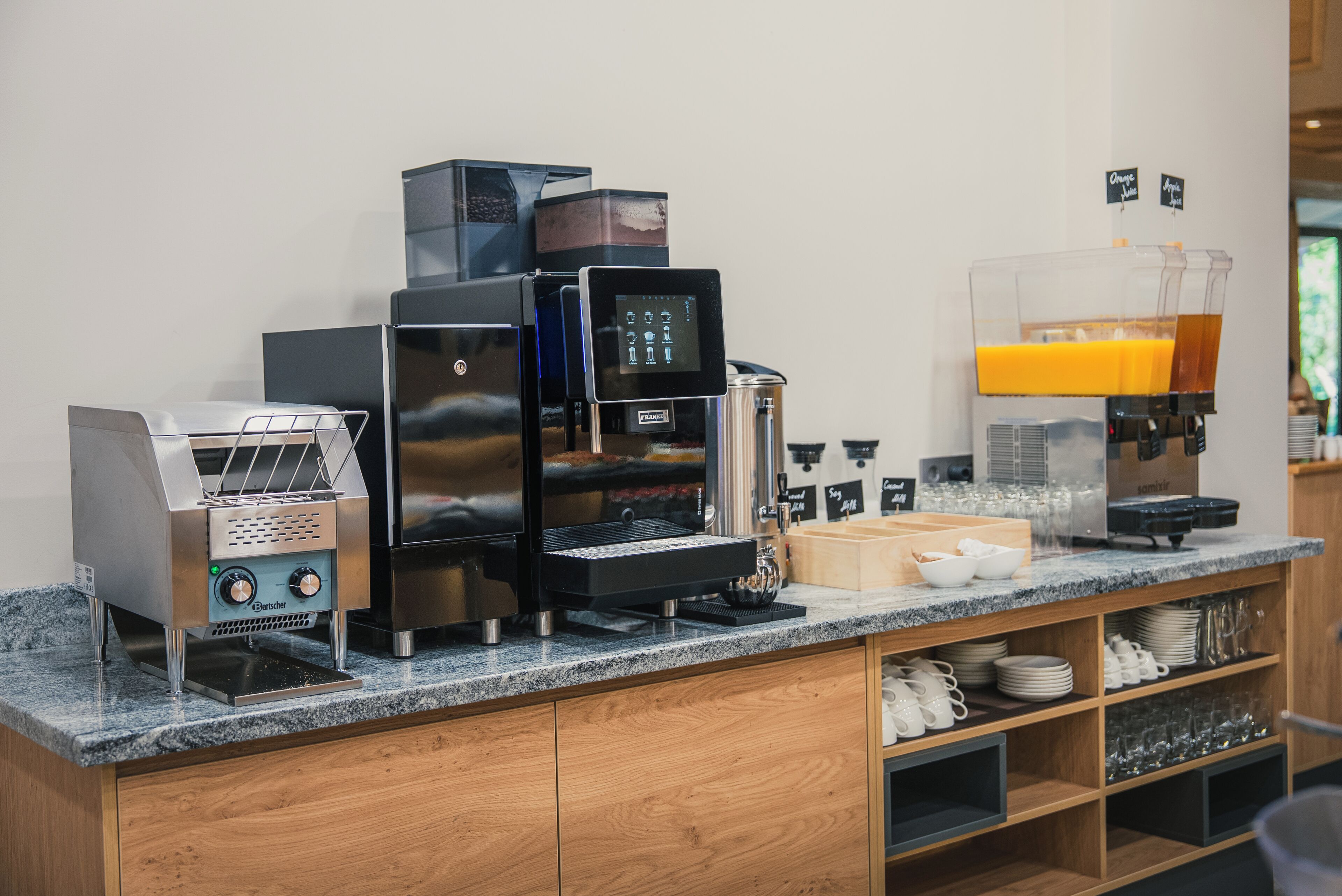 A coffee station with multiple espresso machines, a coffee grinder, and a juice dispenser.