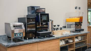 A coffee station with multiple espresso machines, a coffee grinder, and a juice dispenser.