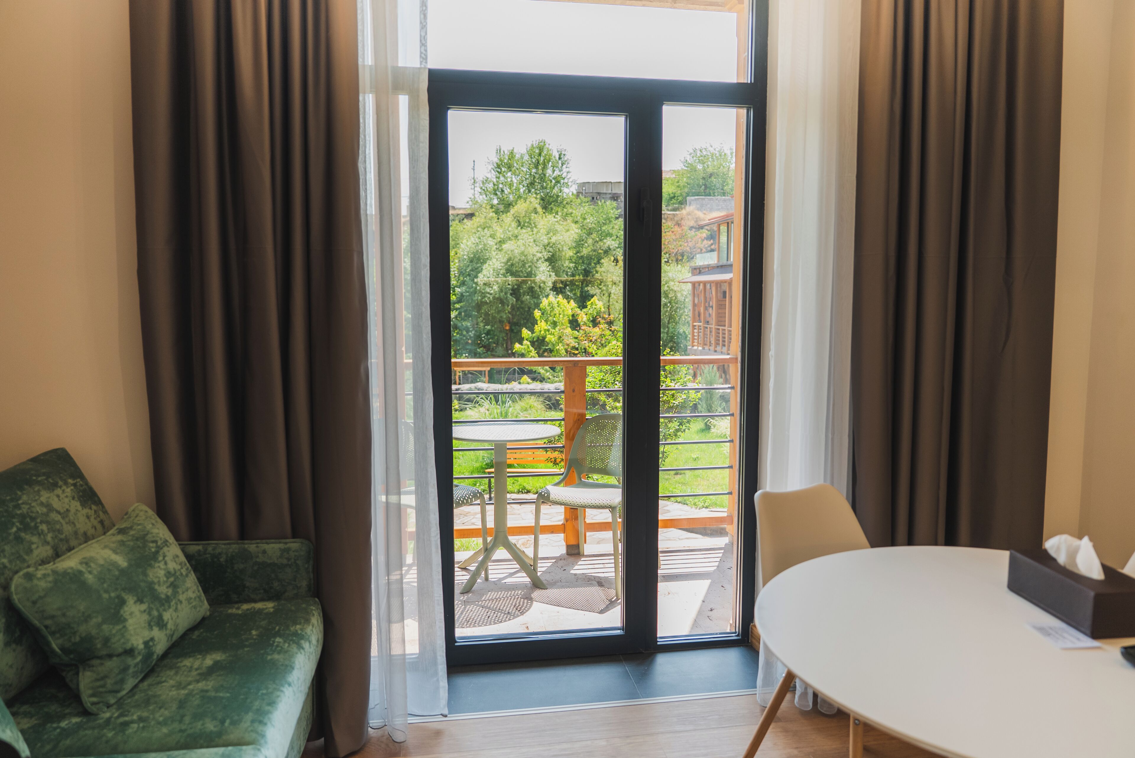 A room with a green sofa, a table, and a view of an outdoor patio with chairs and a table.