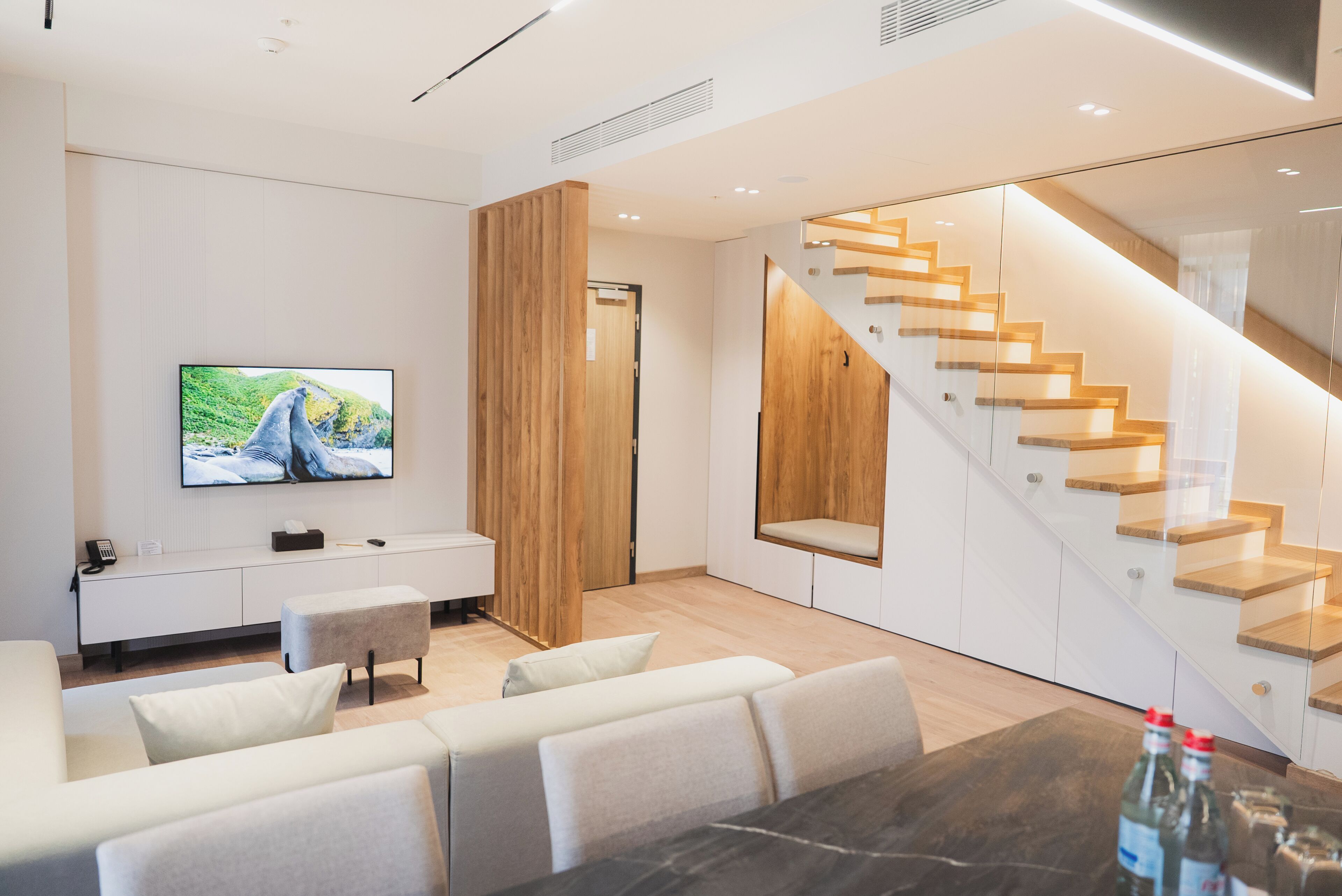Una sala de estar moderna con una televisión de pantalla plana, un sofá, una mesa de centro y una escalera con escalones de madera.