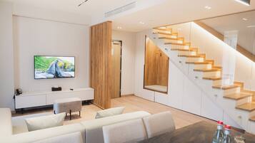 Una sala de estar moderna con una televisión de pantalla plana, un sofá, una mesa de centro y una escalera con escalones de madera.