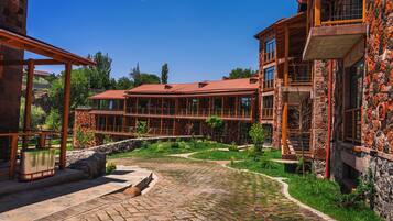 A multi-story building with a stone facade, a red-tiled roof, and a courtyard with a cobblestone pathway.