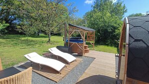 Una terraza de madera con dos sillones, un jacuzzi y un pérgola de madera.