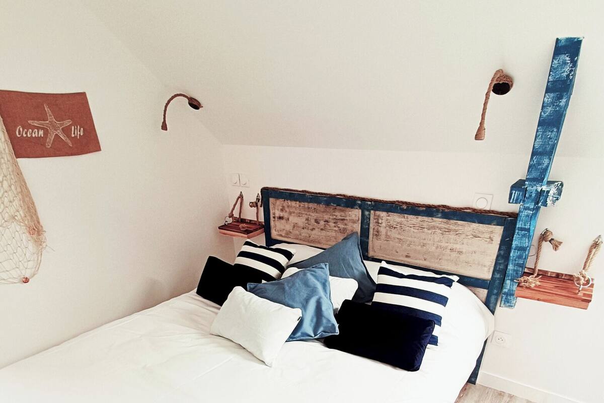 A neatly made bed with striped pillows and a white comforter, a wooden headboard, a small wooden nightstand with a lamp, and a wall-mounted sign that reads "Ocean Life".