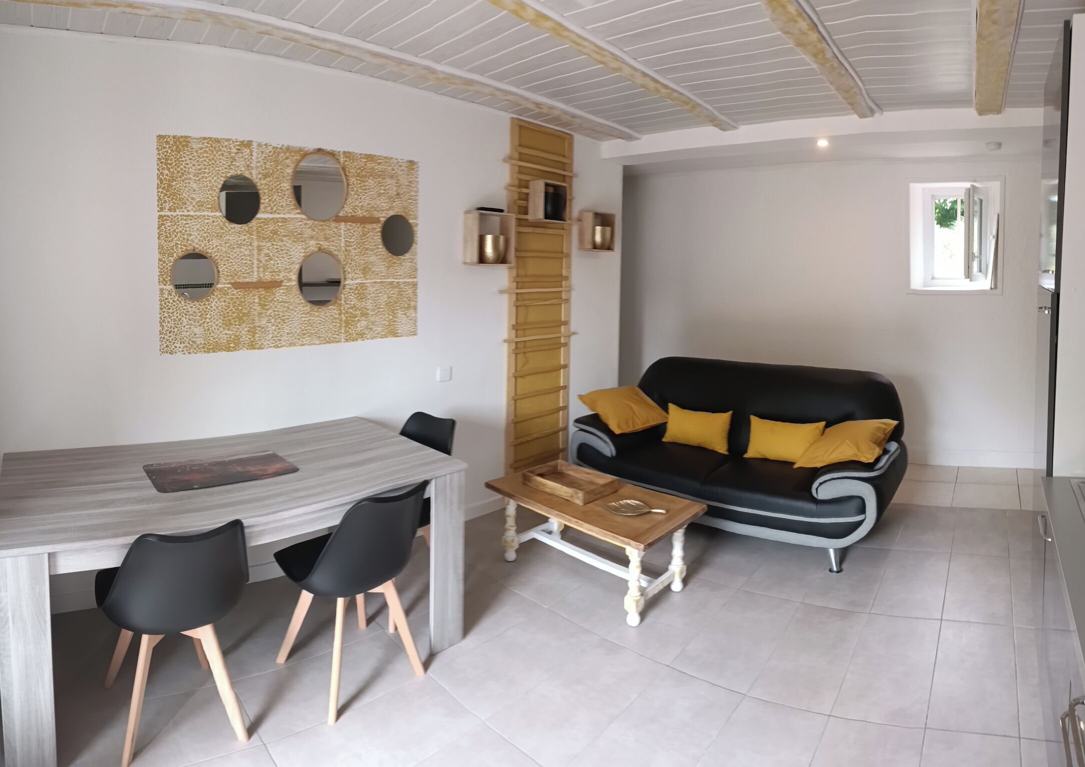 A modern living room with a dining area, featuring a sofa with yellow cushions, a coffee table, and a dining table with chairs.
