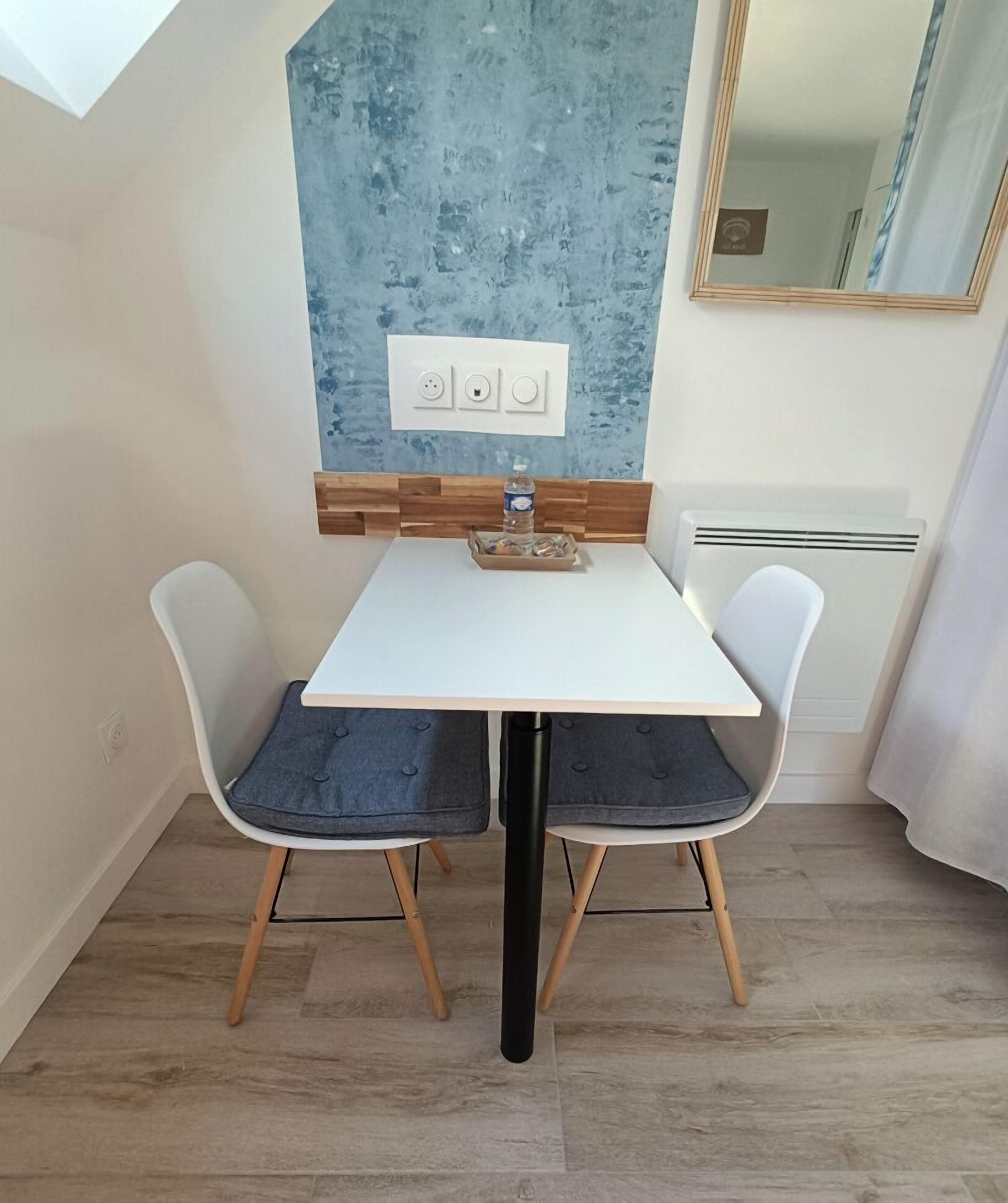 A dining area with a white table and two chairs, a blue textured wall, and a mirror above the table.