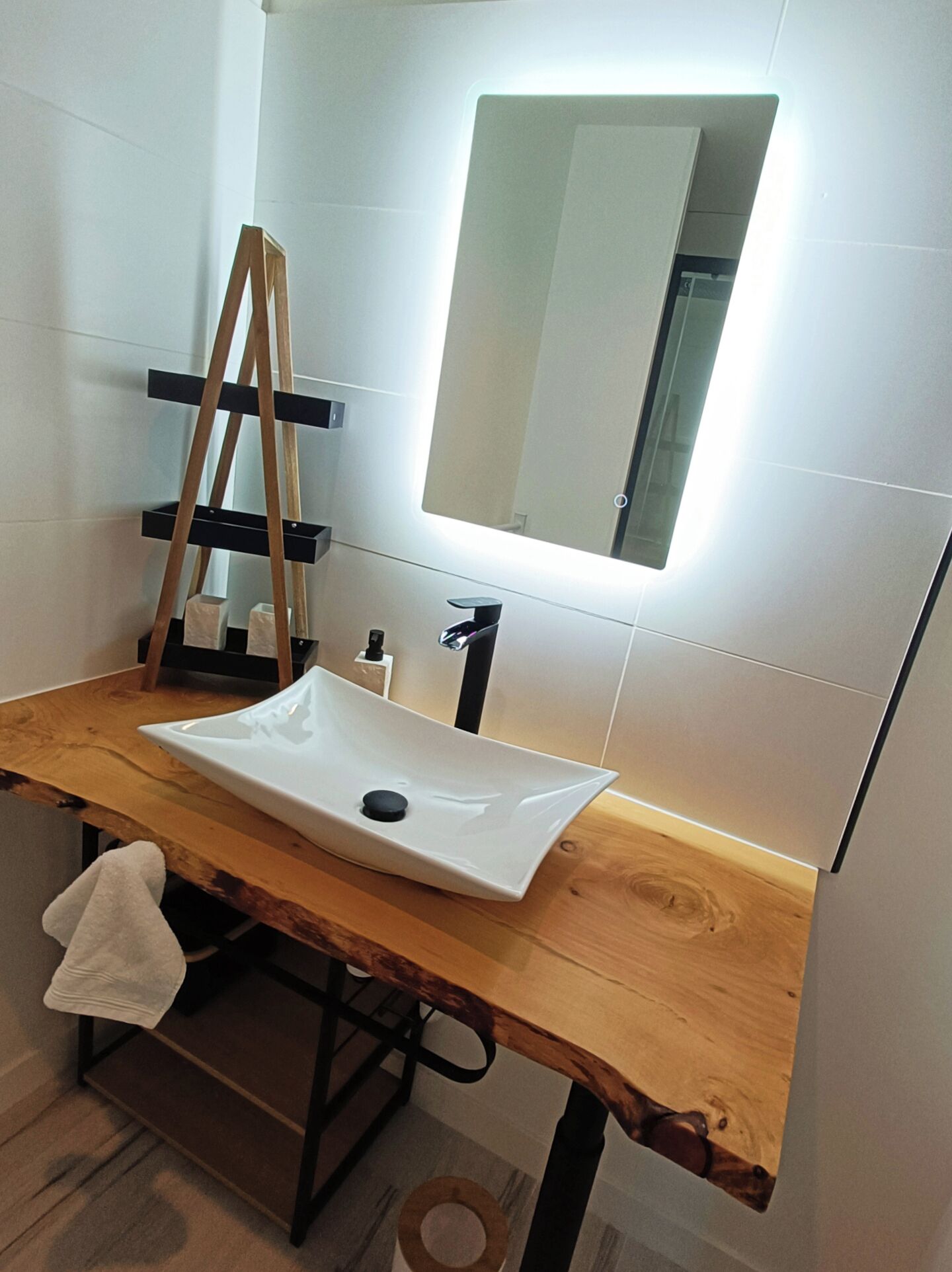 Un baño con tocador de madera, un lavamanos blanco, un espejo y un perchero para toallas.