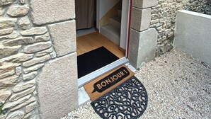 Entrada de un edificio de piedra con puerta de madera, un marco rojo y un felpudo negro que dice "BONJOUR".