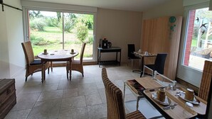 Un área de comedor con mesa y sillas, una estación de café y vistas al jardín a través de amplios ventanales.