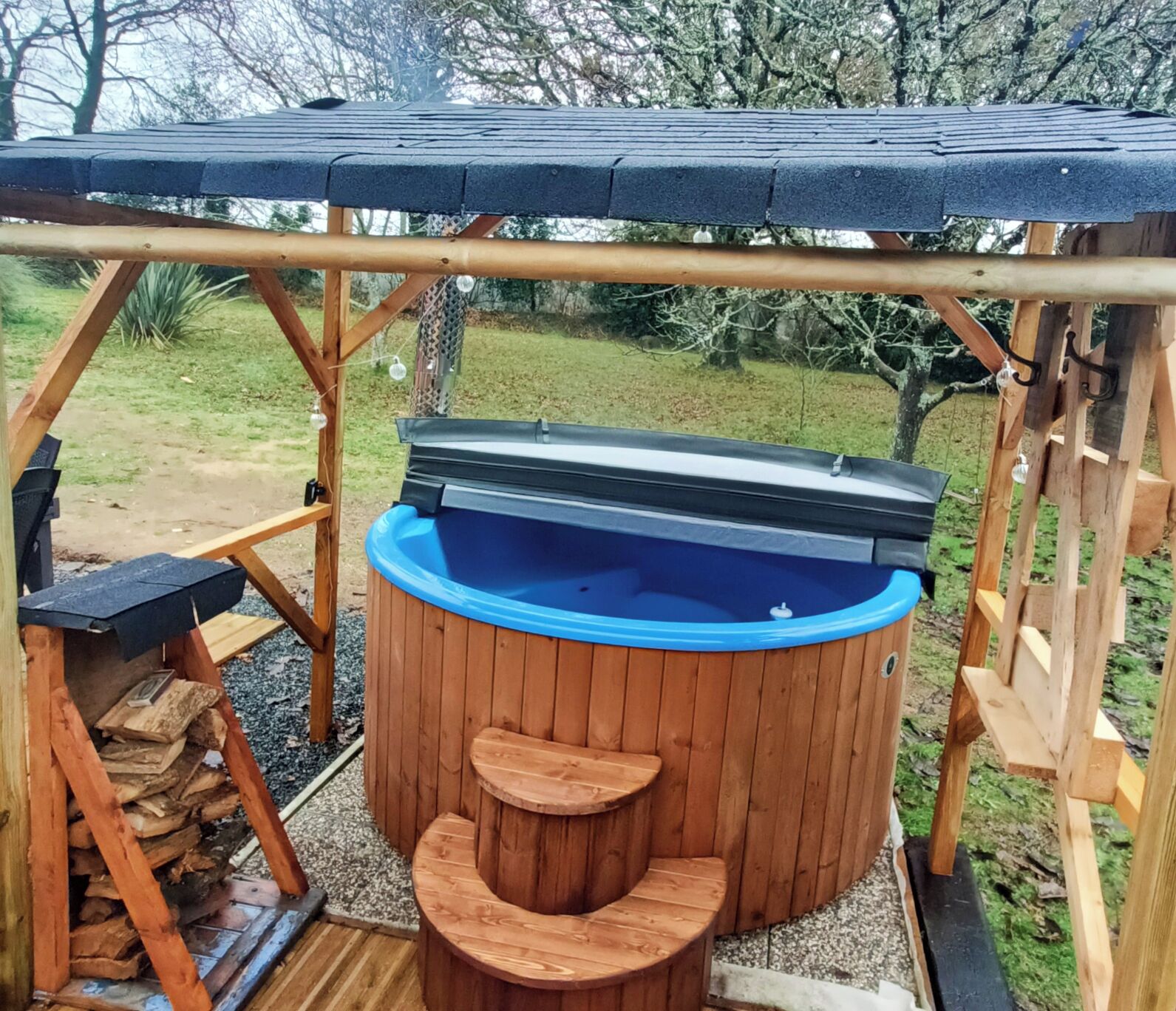 A wooden hot tub with a blue interior, surrounded by a wooden deck and a covered area with a roof.