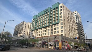 A multi-story hotel with a green and beige facade, multiple balconies, and a ground-level commercial area with shops. - The Time Hotel (Incheon)