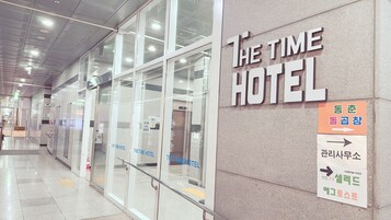 The exterior of The Time Hotel with clear signage, a modern glass facade, and directional arrows for hotel services.
