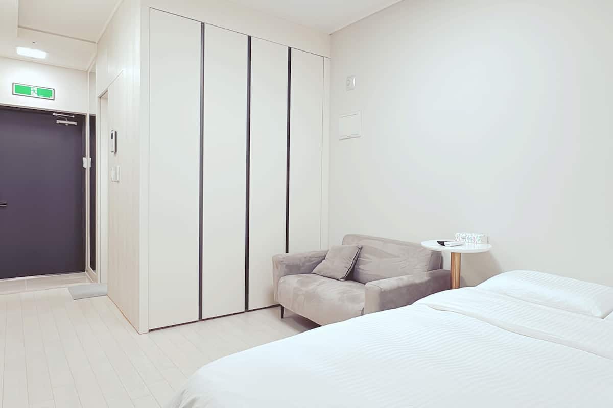 A hotel room with a bed, a chair, a small table, and a wardrobe.